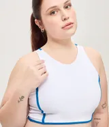 Top deportivo femenino confeccionado en microfibra, de color blanco con vivos en azul, escote redondo, copa y breteles anchos.