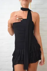 Vestido corto negro de estilo strapless con ajuste drapeado en el torso y falda con volados en capas. Incluye una cinta negra a modo de gargantilla integrada al diseño.