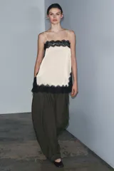 Top lencero de escote recto y tirantes finos, color crema, con aplicación de encaje negro contrastante en todo el contorno. Presenta aberturas laterales en el bajo.