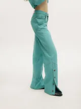 Pantalón de denim color marrón con efecto gastado, tiro medio y corte recto ancho, inspirado en los años 70. Presenta una hilera de botones decorativos en la parte inferior de las piernas.