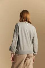 Sweater color crema con mangas abullonadas y puños elastizados. Presenta una textura tejida en relieve con patrón de ladrillos en el cuerpo y rayas horizontales en las mangas.