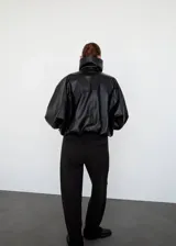 Parka oversize de cuero de piel de ovino color negro, con cuello embudo, solapas amplias y cierre oculto de cremallera y botones. Cuenta con manga larga con puños elásticos y dos bolsillos laterales.