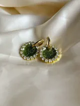 Aros colgantes dorados con dije circular de resina verde brillante, rodeado de strass. El arito es de acero quirúrgico.
