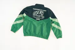 Campera deportiva unisex de nylon liviano, color negro, verde y gris, con paneles diagonales en contraste, calce relajado y estructura clásica. Incluye micrográfico de "encontrame en el under" aplicado al frente y un gráfico en la espalda.