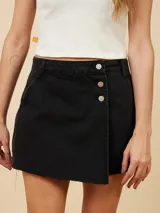 Short pollera de denim negro con diseño cruzado, cierre frontal con botones metálicos y ruedo desflecado.