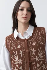 Chaleco tejido color marrón con bordados artesanales de motivos florales y geométricos en color crema. Presenta cuello redondo, cierre frontal con botones y diseño sin mangas.