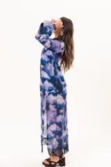 Vestido largo de manga larga con terminación campana, de color azul y violeta con estampado tie-dye, cuello mao con ojal y tajo frontal. Cuenta con flecos en el ruedo y tajo en la pierna.