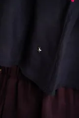 Top corto negro con tirantes finos, escote recto y diseño holgado. Presenta un estampado estilo paisley con detalles en tonos fucsia, turquesa y verde, además de una cenefa geométrica en la parte superior.