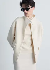 Chaqueta de corte recto confeccionada en mezcla de lana y viscosa, color crema. Presenta cuello alto, cierre frontal con botones ocultos, manga larga y dos bolsillos con solapa en la parte delantera.