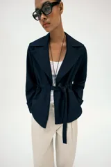 Chaqueta estilo trench corta color azul marino confeccionada con lino. Cuenta con cuello solapa, manga larga con trabilla, bolsillos delanteros de vivo y cierre frontal con lazada ajustable en la cintura.