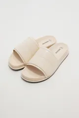 Sandalias planas color marfil, con tira ancha acolchada en el empeine y suela baja con borde oscuro.