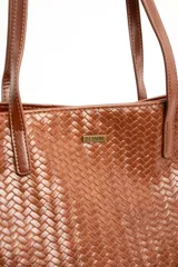 Bolso tipo shopper color marrón de cuero sintético con diseño trenzado. Cuenta con doble asa de hombro y placa metálica con el logo de la marca en el frente.