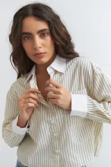 Camisa de manga larga con cuello y puños blancos contrastantes. El cuerpo de la camisa es de color crema con finas rayas verticales azules y tiene un corte crop.