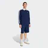 Polo de rugby Adidas de manga larga, color azul marino con cuello y botones blancos. Presenta las icónicas tres tiras blancas en los hombros y mangas, y el logo del trifolio bordado en el pecho.