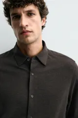 Camisa de corte relajado confeccionada en tejido de algodón con textura. Presenta cuello italiano, manga larga con puños abotonados y cierre frontal mediante botonadura.