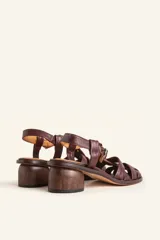 Sandalias de cuero color negro con diseño de tiras cruzadas tipo huarache, tira ajustable con hebilla metálica en el empeine y taco cilíndrico de madera.
