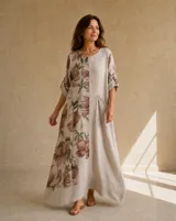 Vestido largo beige, con diseño de corte recto y holgado. Cuenta con un panel frontal con un gran estampado floral en tonos marrones y verdes, escote redondo, mangas tres cuartos con trabilla y un bolsillo aplicado en el frente.
