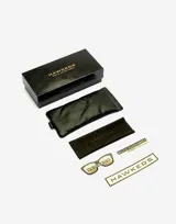 Lentes de sol Hawkers unisex, modelo Paula Echevarría Rubin, con montura negra y lente espejada gris con detalle dorado en la parte superior.