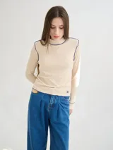 Polera de cuello alto confeccionada en tela rib color blanco, con mangas largas y hombreras. Presenta pespuntes en contraste en las terminaciones del cuello, hombros y puños.