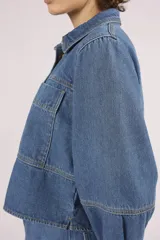 Camisa de denim celeste, de corte cropped, con cuello camisero, mangas 3/4 abullonadas y cierre frontal con botones.