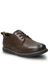 Zapato casual Hush Puppies modelo Bolo, confeccionado en cuero color marrón oscuro. Presenta cierre con cordones, suela de EVA flexible y diseño estilizado con costuras visibles en el borde de la suela.