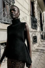 Top de punto color verde militar, con cuello subido y manga sisa. Presenta apliques dorados en los laterales y un bajo asimétrico.