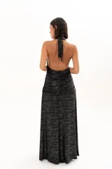 Vestido largo de fiesta con escote halter profundo y espalda descubierta. Presenta un diseño drapeado en la zona central del torso y una falda fluida con tajo lateral. Confeccionado en tejido con acabado brillante tipo lurex.