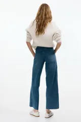 Jean tobillero de denim azul con leve stretch, tiro alto y piernas amplias de corte ancho. Presenta bolsillos de parche delanteros con botón y pliegues marcados.