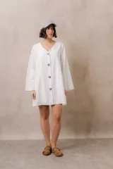 Vestido corto blanco de corte amplio y relajado, con escote en V, mangas largas amplias y botones frontales a contratono.