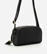 Cartera pequeña de hombro marca Satinato, confeccionada en PU con textura granulada. Presenta doble compartimento con cierre de cremallera metálica dorada, correa larga ajustable y un dije decorativo metálico con el logo de la marca.