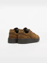 Championes Veja modelo V-90 Suede, confeccionados íntegramente en gamuja de color marrón coñac. Presentan puntera perforada, cordones tono sobre tono, suela de goma marrón y la clásica 'V' de la marca en el lateral con el mismo material y tono. Incluyen detalles de la marca grabados en el talón.