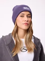 Gorro tipo beanie de tejido acanalado en color violeta, con parche rectangular bordado con el logo de la marca Rusty en el frente.