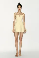Vestido corto color amarillo pálido, con escote corazón, tirantes finos ajustables con detalle de lazos y falda acampanada.