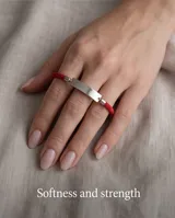 Pulsera de cordón rojo con chapa de identidad en acero y terminales metálicas.