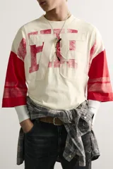 Camiseta boxy fit de cuello redondo y manga por debajo del codo. Presenta un diseño bicolor en tonos blanco off-white y rojo, con estampado y parches frontales con efecto lavado vintage y franjas en las mangas.