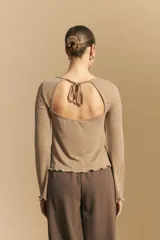 Top negro de manga larga acampanada con escote pronunciado en la espalda que se ajusta con lazos. La tela presenta una textura sutil con brillo, similar a un animal print discreto.