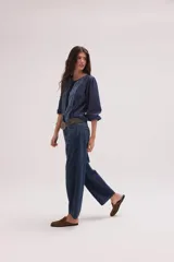 Blusa de jean fino de algodón azul, con escote a la base, mangas abullonadas y puños elásticos. Cuenta con pechera decorada con cintas superpuestas de efecto rústico y desmechado.