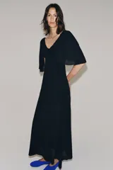 Vestido largo de punto color negro, con escote en V pronunciado tanto en el delantero como en la espalda, y mangas cortas anchas con vuelo.