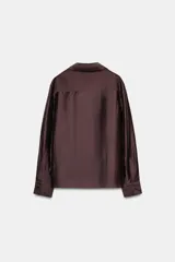 Camisa de manga larga color marrón oscuro, con cuello solapa, escote pico y bajo asimétrico. Presenta un bolsillo plastrón en el delantero con bordado combinado a tono.