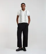 Camisa polo slim de punto, color blanco con rayas verticales oscuras en contraste en el frente y líneas en los bordes de las mangas cortas. Cuenta con cuello polo y cierre frontal parcial con cremallera.