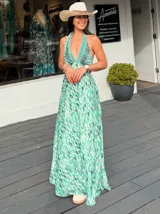 Vestido largo con estampado de hojas en tonos verde y blanco, con escote halter y espalda descubierta.