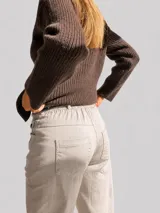 Pantalón de corte recto y holgado en color beige, con cintura elástica y dobladillo en los tobillos. Incluye un cinturón de cuero sintético con tachas metálicas decorativas.