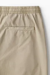 Pantalón de algodón color beige, estilo casual con corte relajado, cintura elástica con cordón de ajuste oculto y bolsillos al bies y traseros.