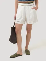Short de lino orgánico color beige, de tiro medio y calce holgado, con detalles de aberturas bordadas en la cintura y en los dobladillos. Cuenta con bolsillos laterales y pinzas frontales.