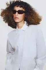 Camisa de algodón con estampado de rayas verticales, cuello solapa y puños en color blanco a contraste. Presenta cierre frontal con botones, bolsillo de plastrón en el delantero y bajo asimétrico.