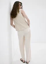 Pantalón de tiro alto color crudo, con diseño largo y corte recto. Cuenta con trabillas, bolsillos laterales y cierre frontal oculto con cremallera, botón y ganchos.