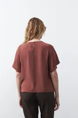 Top negro de manga corta con detalle de nudo en el escote y abertura tipo gota. Presenta una silueta relajada y textura sutil en la tela.