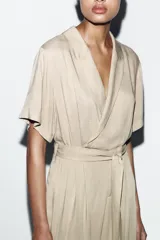 Mono largo de cuello solapa y escote en pico cruzado, con mangas cortas. Presenta bolsillos laterales de plastrón con solapa y botones, y un cinturón del mismo tejido para ajustar en la cintura. Cierre frontal con cremallera y botón interior.