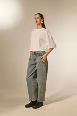 Remera blanca de corte holgado con mangas 3/4 y cuello redondo a la base. Presenta un diseño con apliques de studs metálicos distribuidos por toda la prenda.