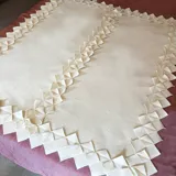 Manta de lana afieltrada color crema, con terminaciones decorativas de figuras geométricas.